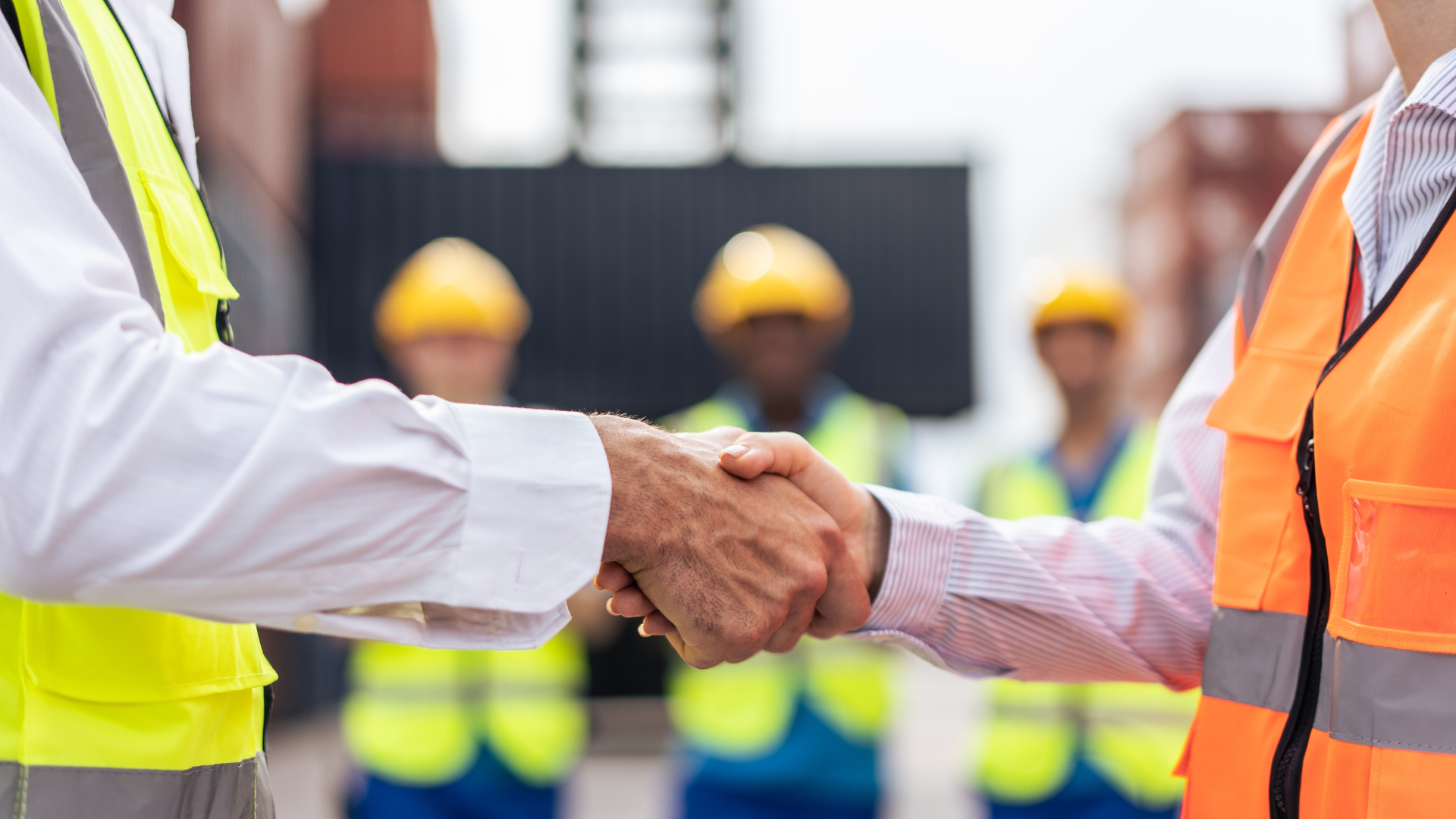 Zwei Hände, die sich schütteln mit Team im Hintergrund in der Produktion